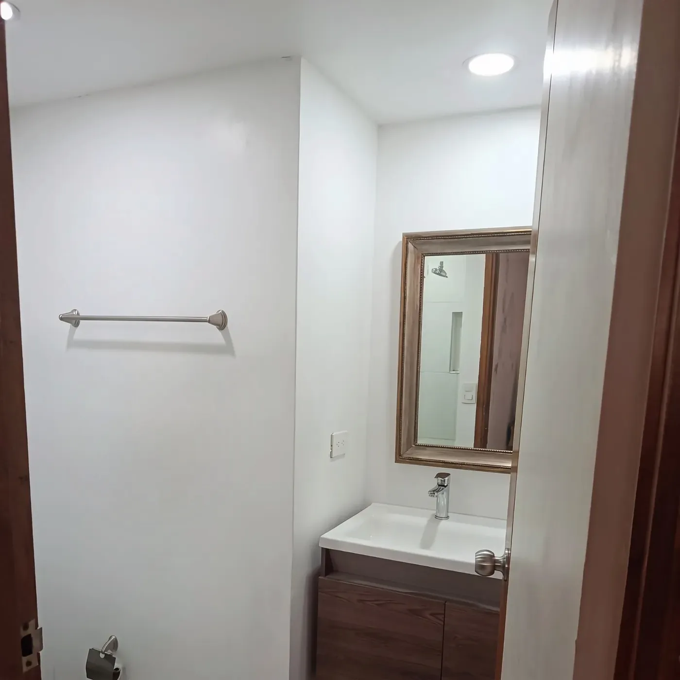 Baño de paredes blancas con un mueble flotante de madera bajo el lavamanos.