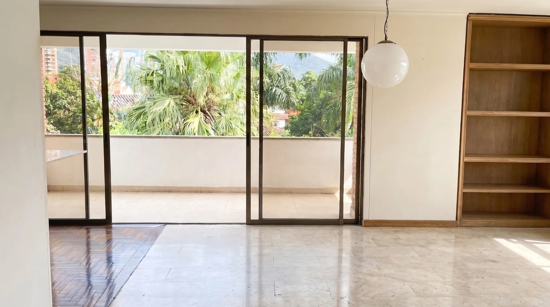 Comedor vacío frente a una puerta corrediza de vidrio abierta a la terraza, con palmas afuera.