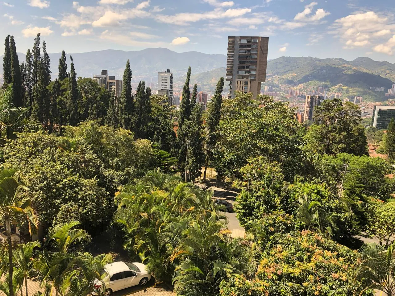 Vista desde el apartamento: cipreses, una torre y la montaña bajo un cielo con nubes.